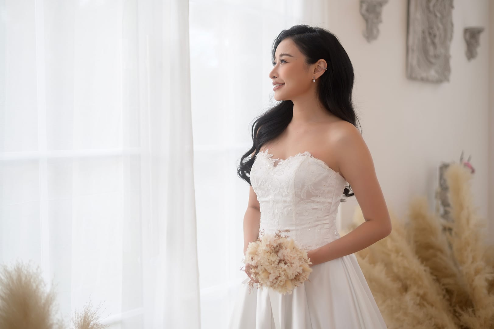 Bride in elegant wedding dress standing at window side profile shot