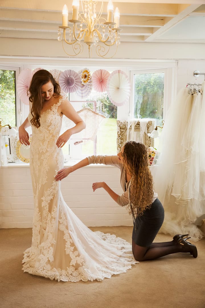 A dressmaker taking in a wedding dress, pinning and fitting it to the client, a young woman. A bride selecting her dress in a specialist shop
