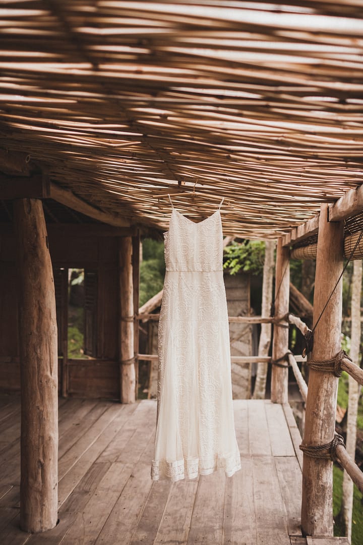 White wedding dress hanging in tropical bamboo house in morning.
