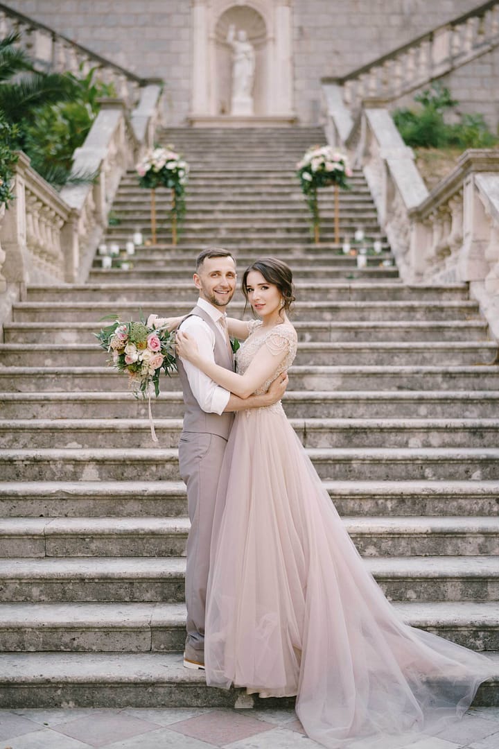 Bride is embracing groom on the stone steps near the old villa