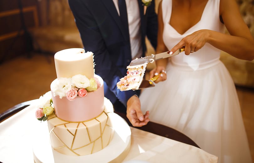 Happy bride and a groom is cutting their stylish wedding cake on wedding banquet. Sweet cake for couple.