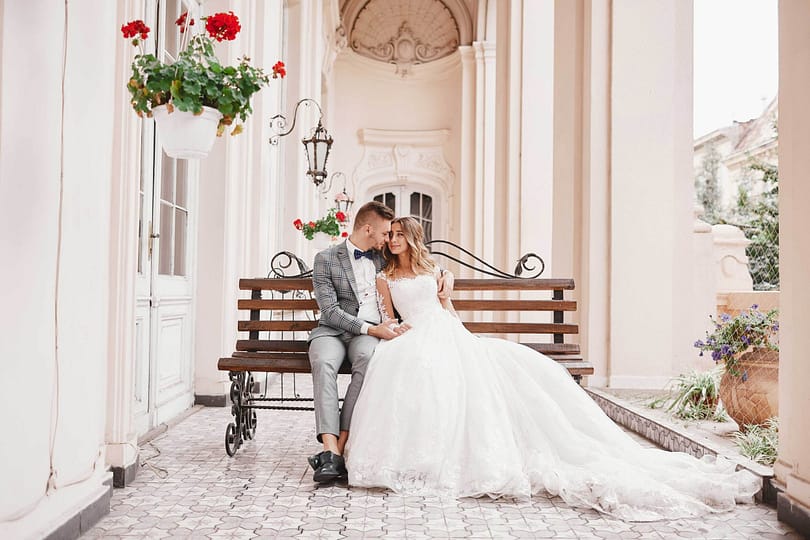 wedding day. beautiful bride in white long dress and young groom wearing in black suit are hugging in historic europe town