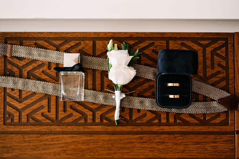 Bottle of men perfume, suspenders, a boutonniere and wedding rings lie on a wooden carved table