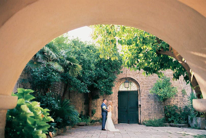 View from the arch to the hugging bride and groom in the courtyard of an ancient building